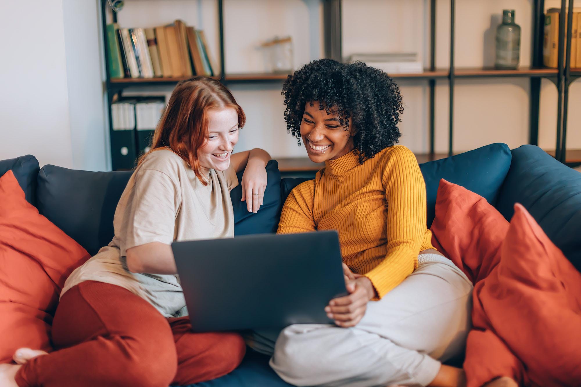 female multiethnic friends on couch watching movie - women flatmates surfing internet together